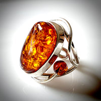 The photograph features a large oval amber ring with two round beads on each side.