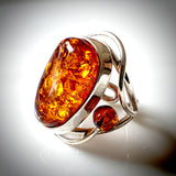 The photograph features a large oval amber ring with two round beads on each side.